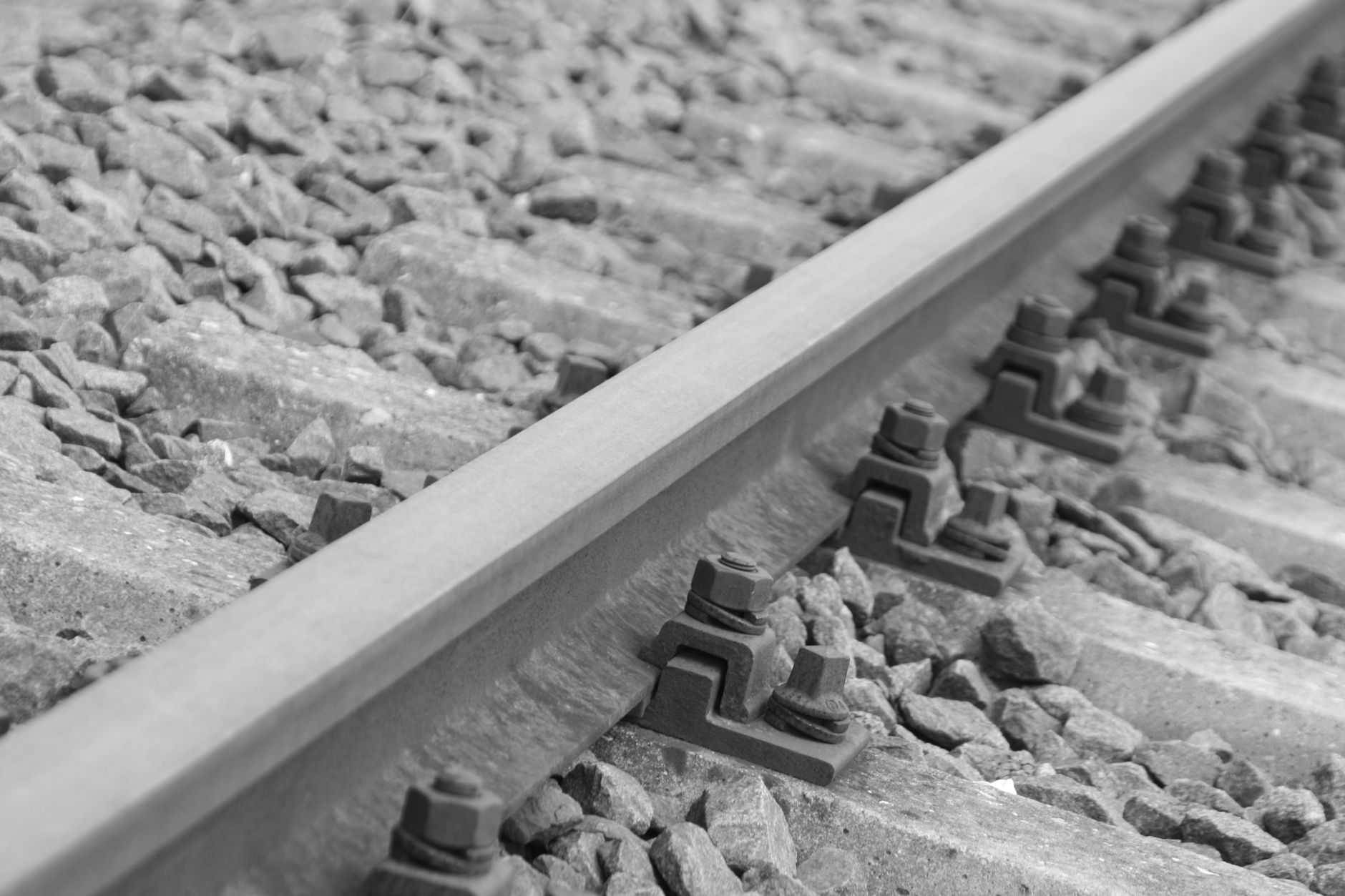 black metal bolts in silver metal train rail track surrounder by gray stones